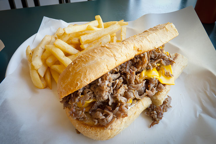 A cheese steak with American cheese and french fries. Perfection on a plate.